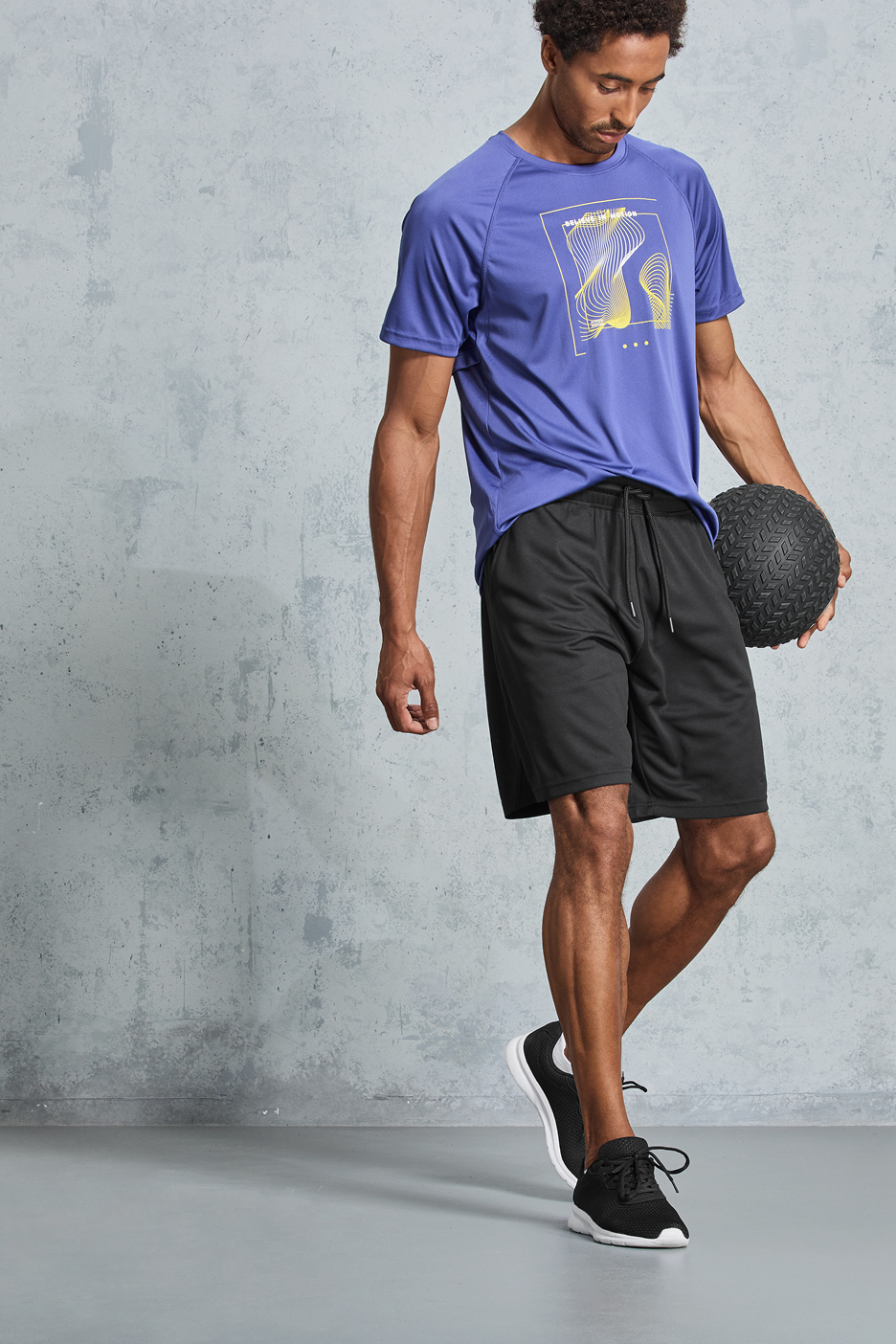 Man i lila t-shirt och svarta shorts med en medicinboll.