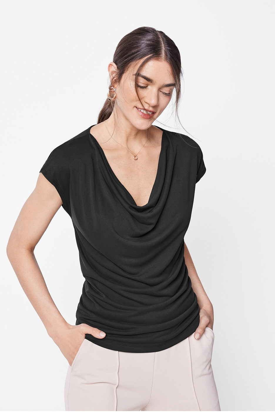 Kvinna i svart topp med draperad halsringning och ljusa byxor.