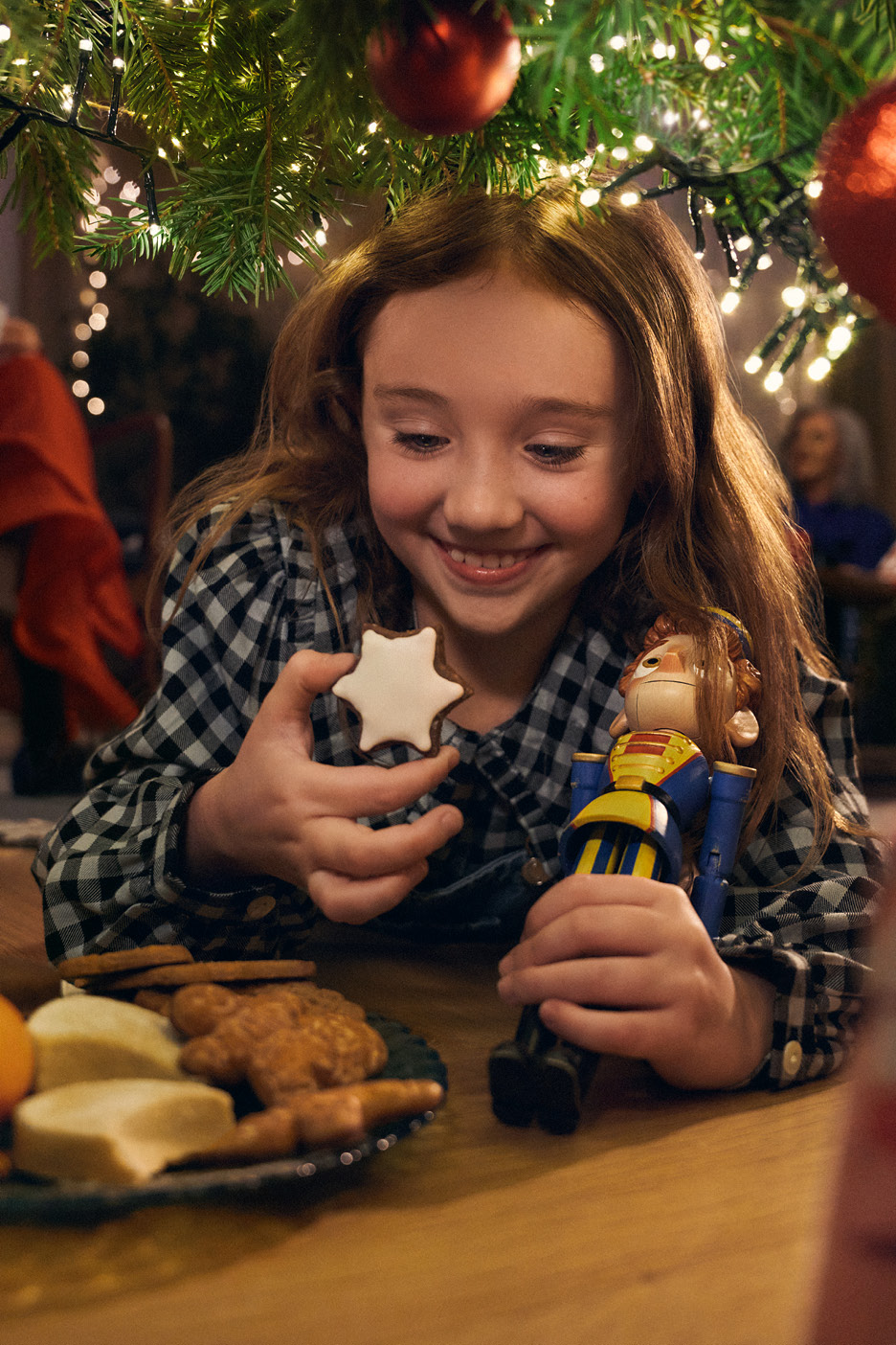 En flicka under julgranen med en pepparkaka och en nötknäppare.