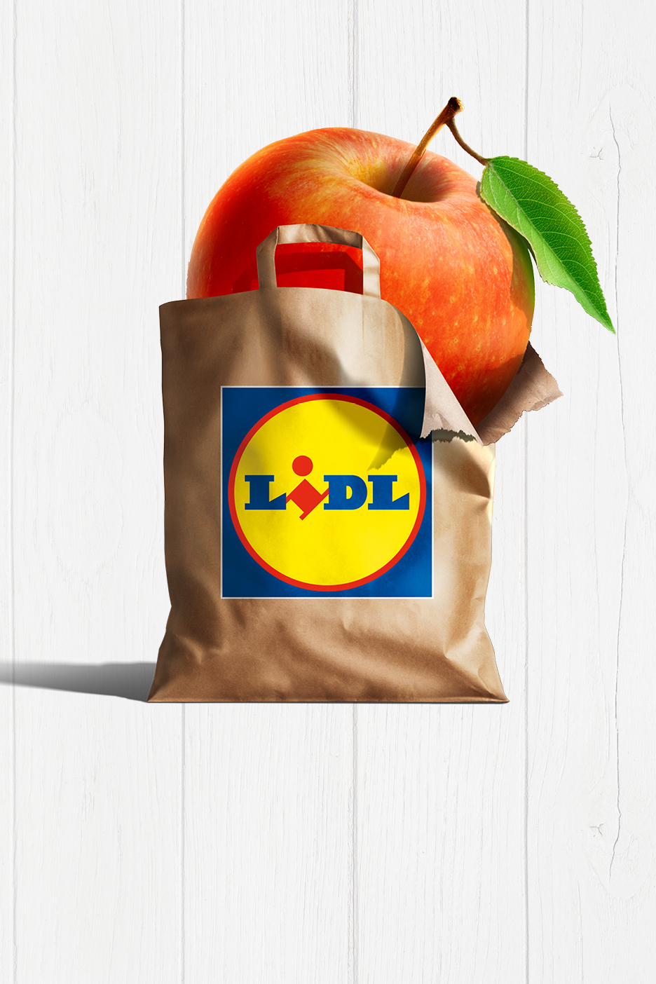 Ett stort rött äpple sticker upp ur en brun papperspåse på en vit träbakgrund.
