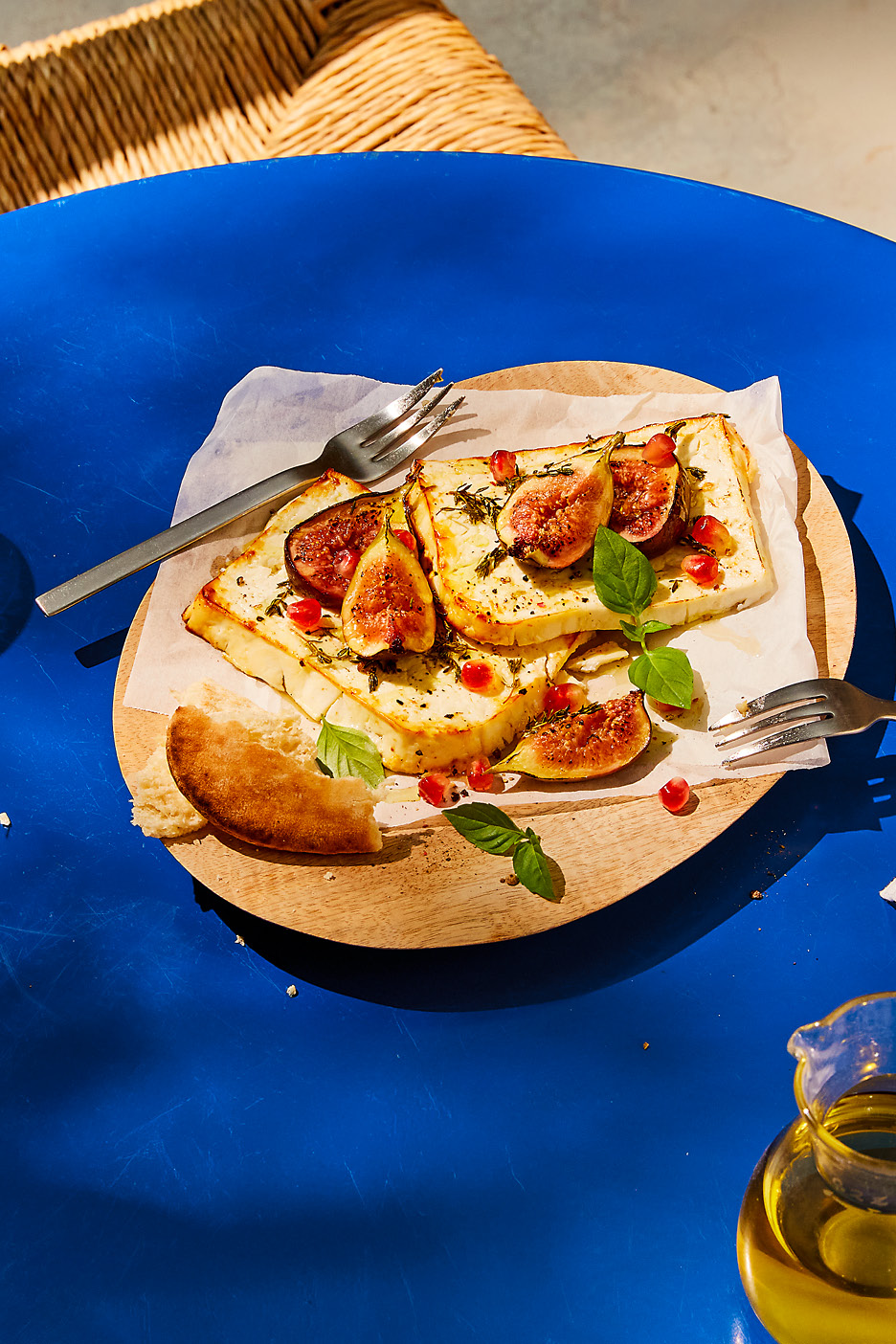 Ugnsbakad fetaost med fikon, granatäpple och basilika på en träskiva med bröd och olivolja.