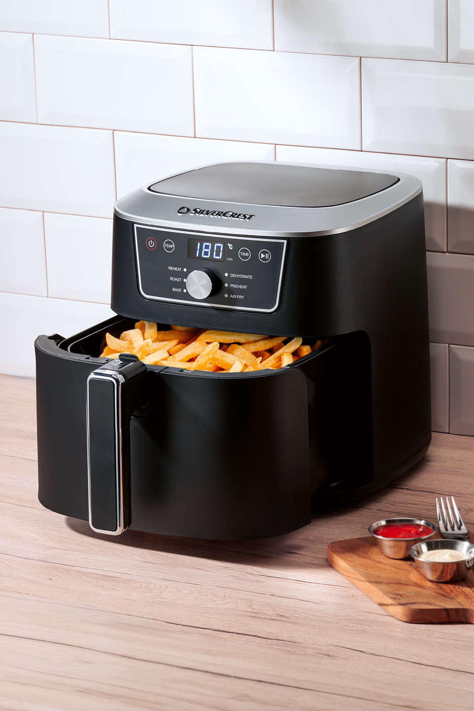 En svart Silvercrest airfryer fylld med pommes frites, med dippsåser och en gaffel bredvid.