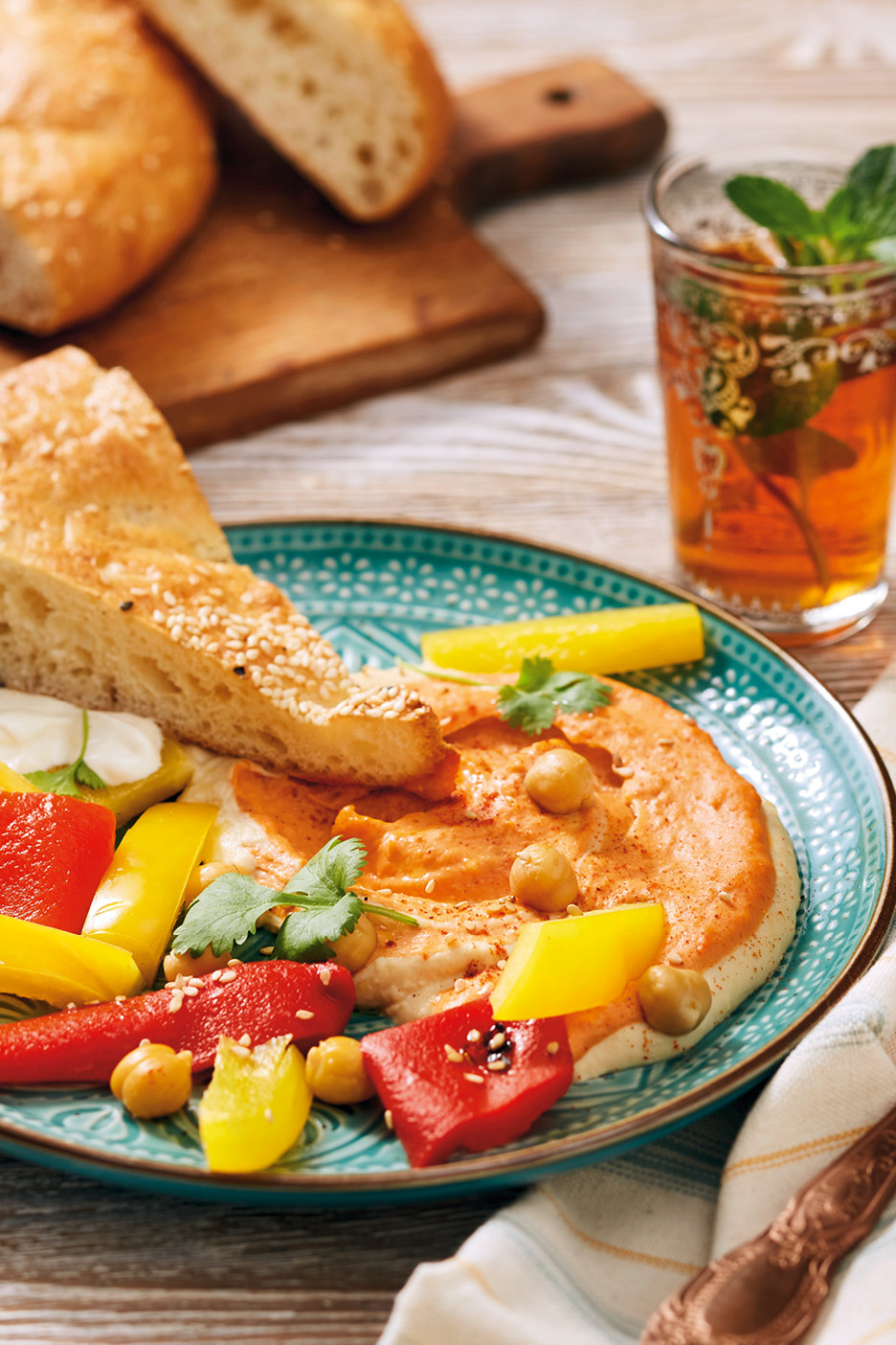 Hummus med paprika, kikärtor, bröd och myntate på ett turkost fat.