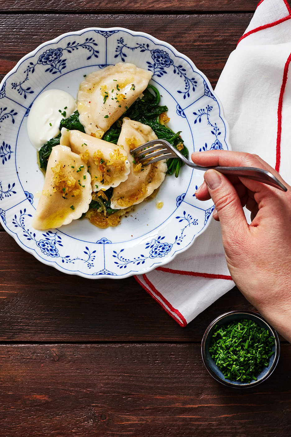 En tallrik med pierogi, spenat och gräddfil, med en hand som håller en gaffel.