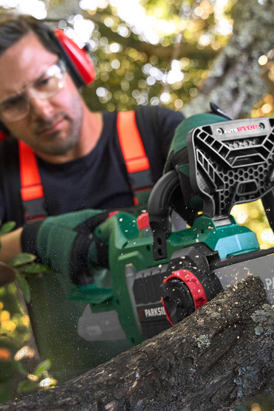 Man med hörselskydd och skyddsglasögon sågar en gren med en motorsåg.