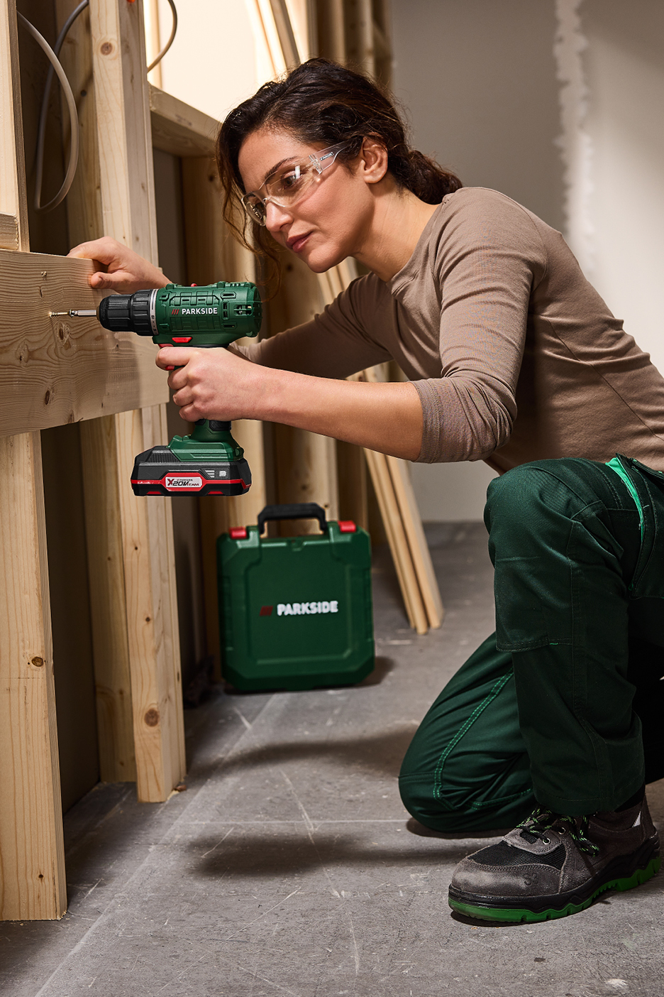 Kvinna med skyddsglasögon använder en sladdlös borrmaskin för att skruva i trä.