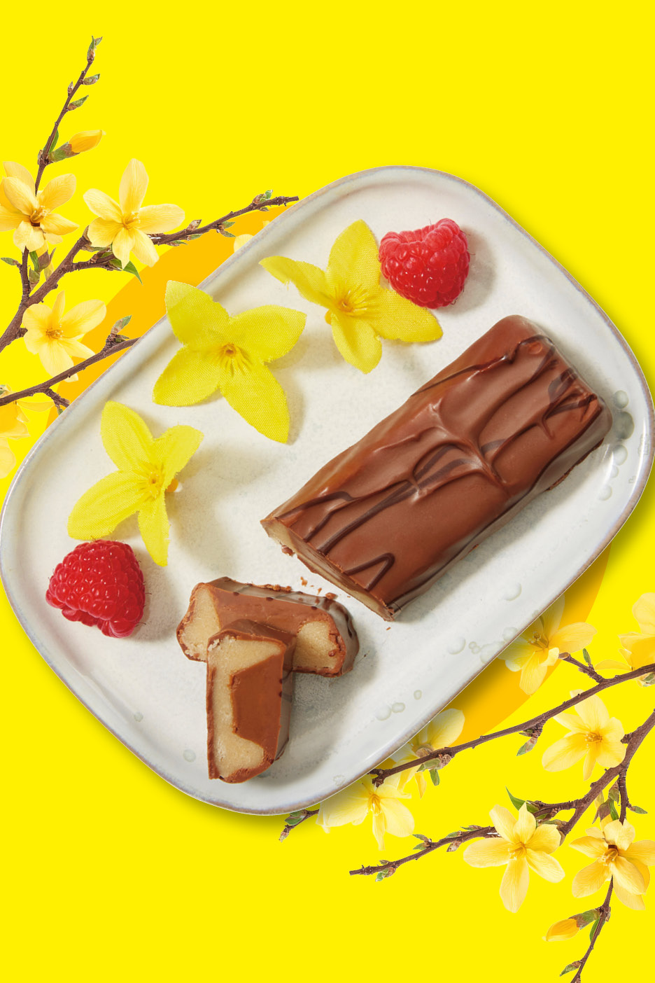 Chokladöverdragna marsipanbitar med hallon och gula blommor på en vit tallrik.