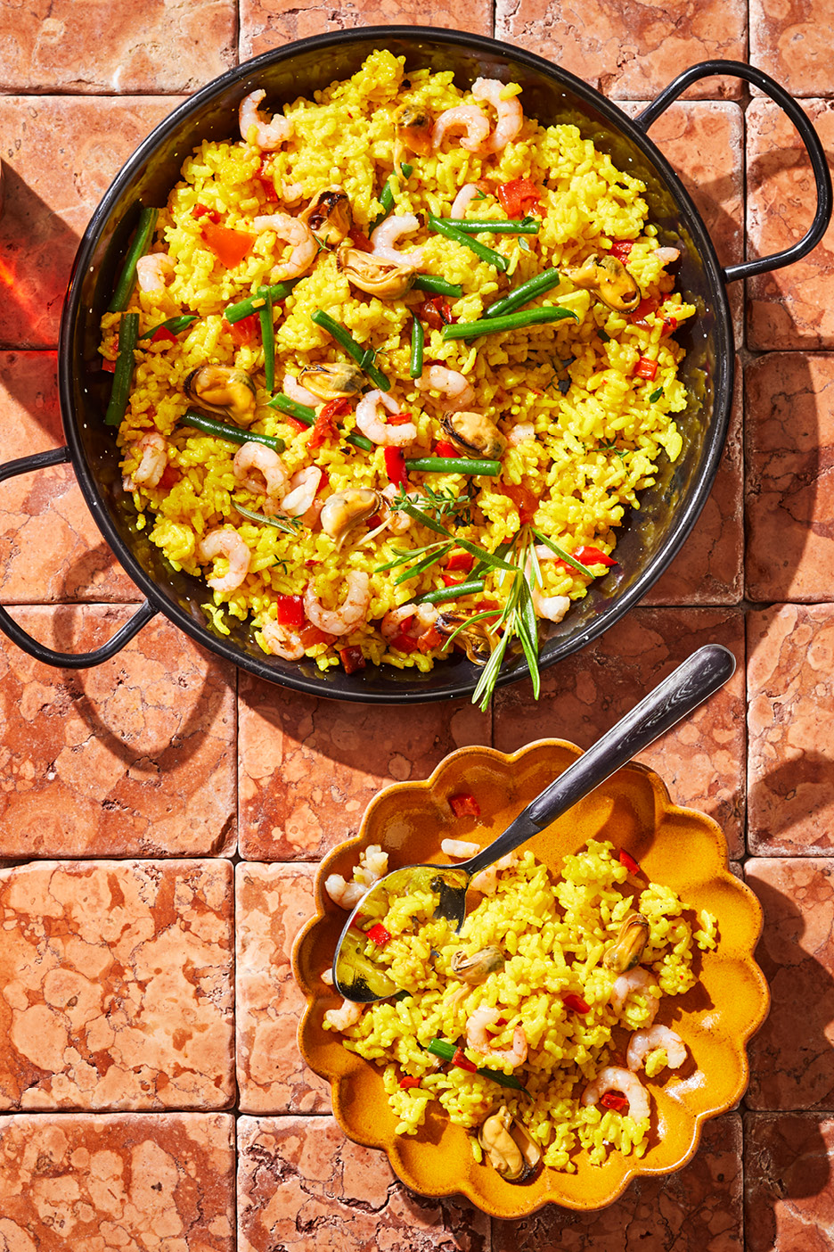 Paella med räkor, musslor, gröna bönor och röd paprika i en stor panna och en skål.