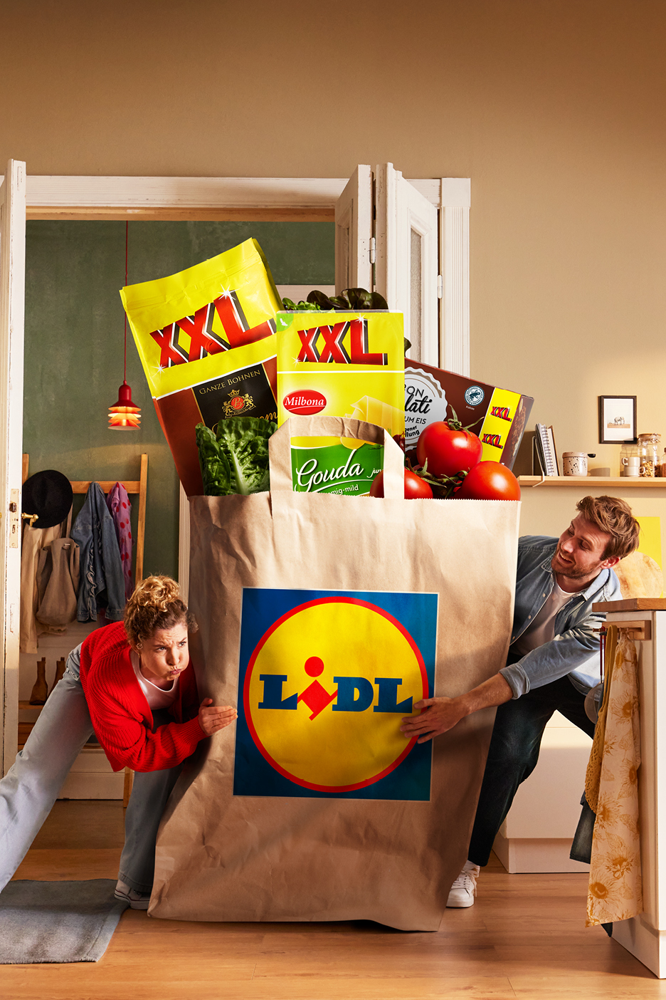 Ett par bär en enorm papperskasse fylld med matvaror, inklusive XXL-kaffe, ost och tomater.