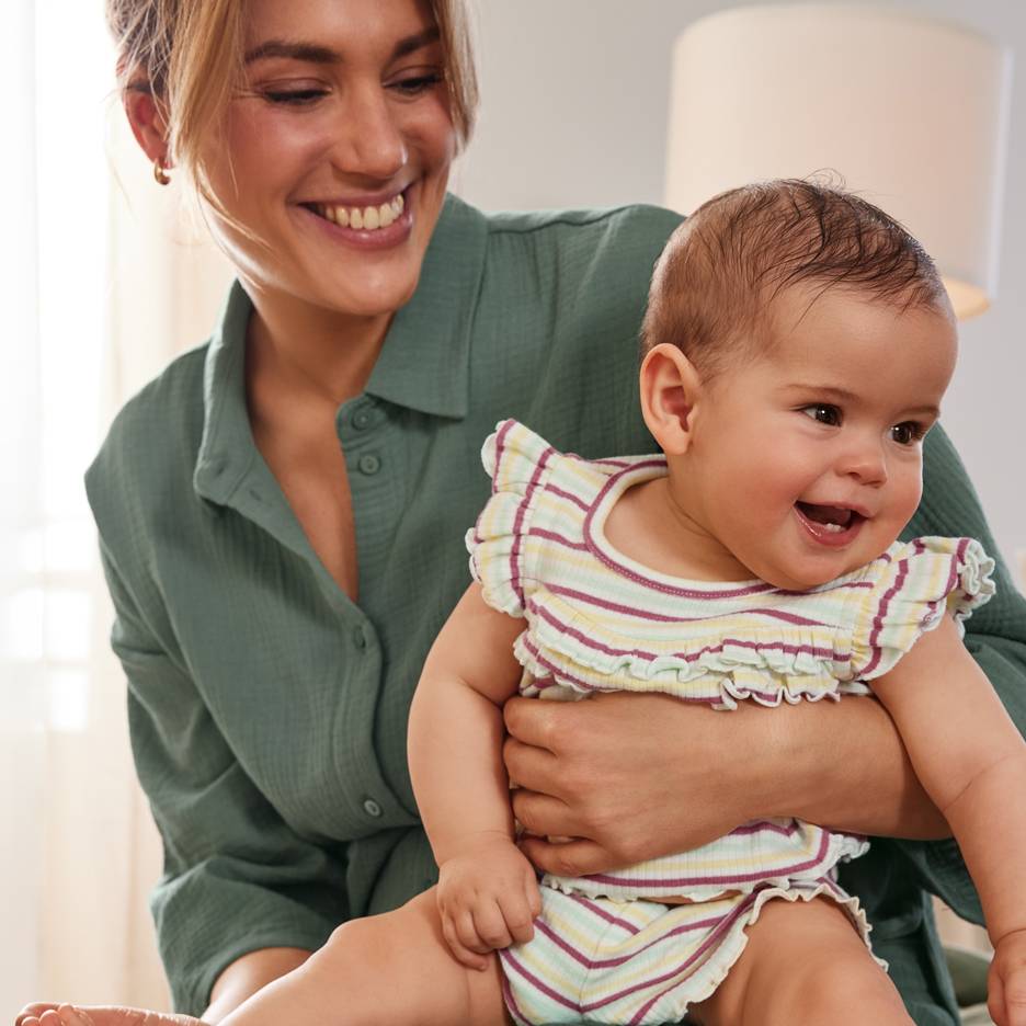 Leende mamma med glad bebis i färgglad randig outfit.