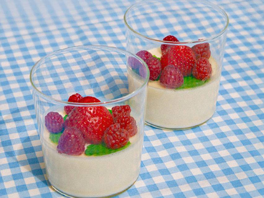 Två glas med krämig pannacotta garnerad med färska jordgubbar och hallon.