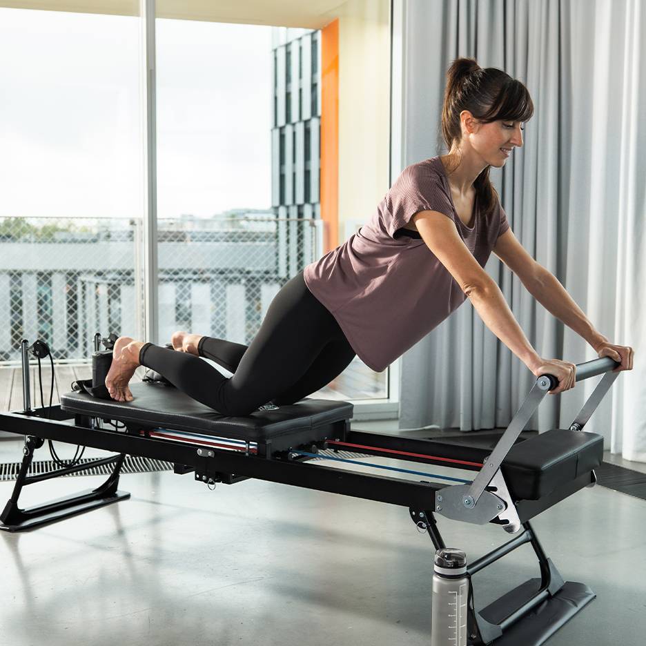 Kvinna tränar pilates på en reformer med fjädrar och remmar.