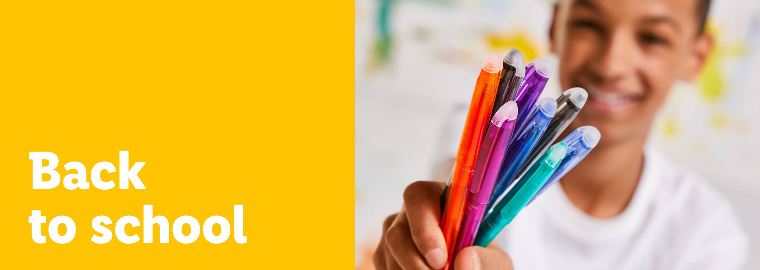 En leende pojke håller en samling färgglada pennor med texten 'Back to school'.