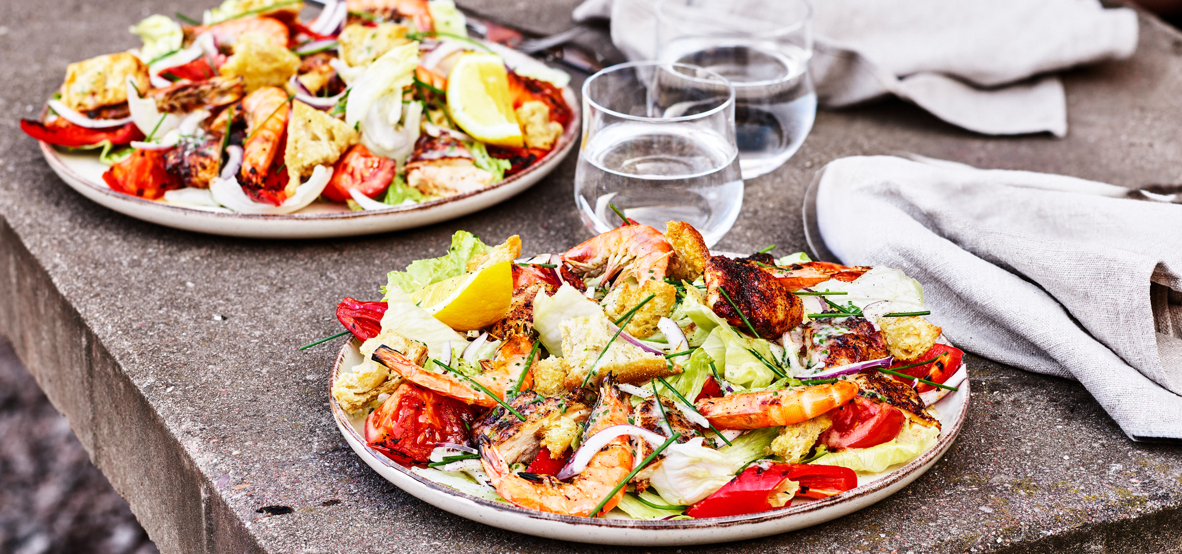 Caesarsallad med grillad kyckling, räkor, krutonger, sallad, tomat, lök och citronklyfta.