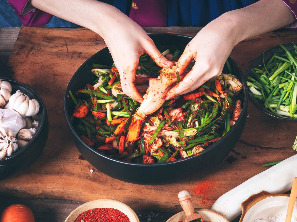 Händer som blandar kimchi med vitlök, salladslök och chilipulver på en träskiva.
