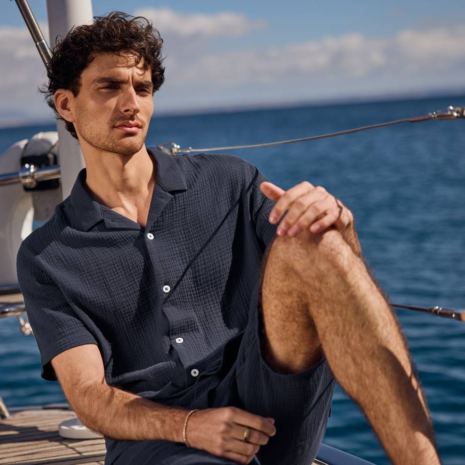 Man i mörkblå skjorta och shorts på en yacht, tittar ut över havet.