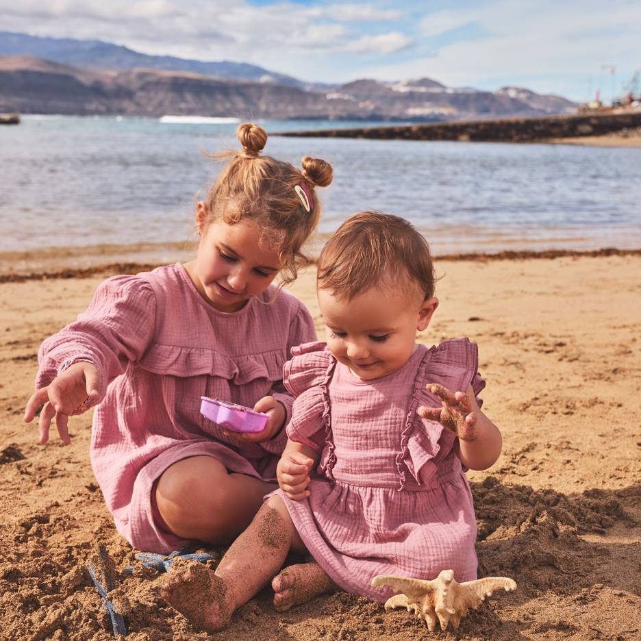 Två flickor i rosa klänningar leker i sanden på stranden.