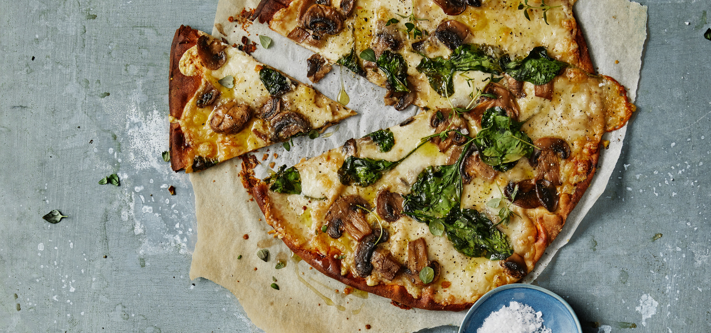 En läcker pizza med champinjoner, spenat och ost, serverad på bakplåtspapper.