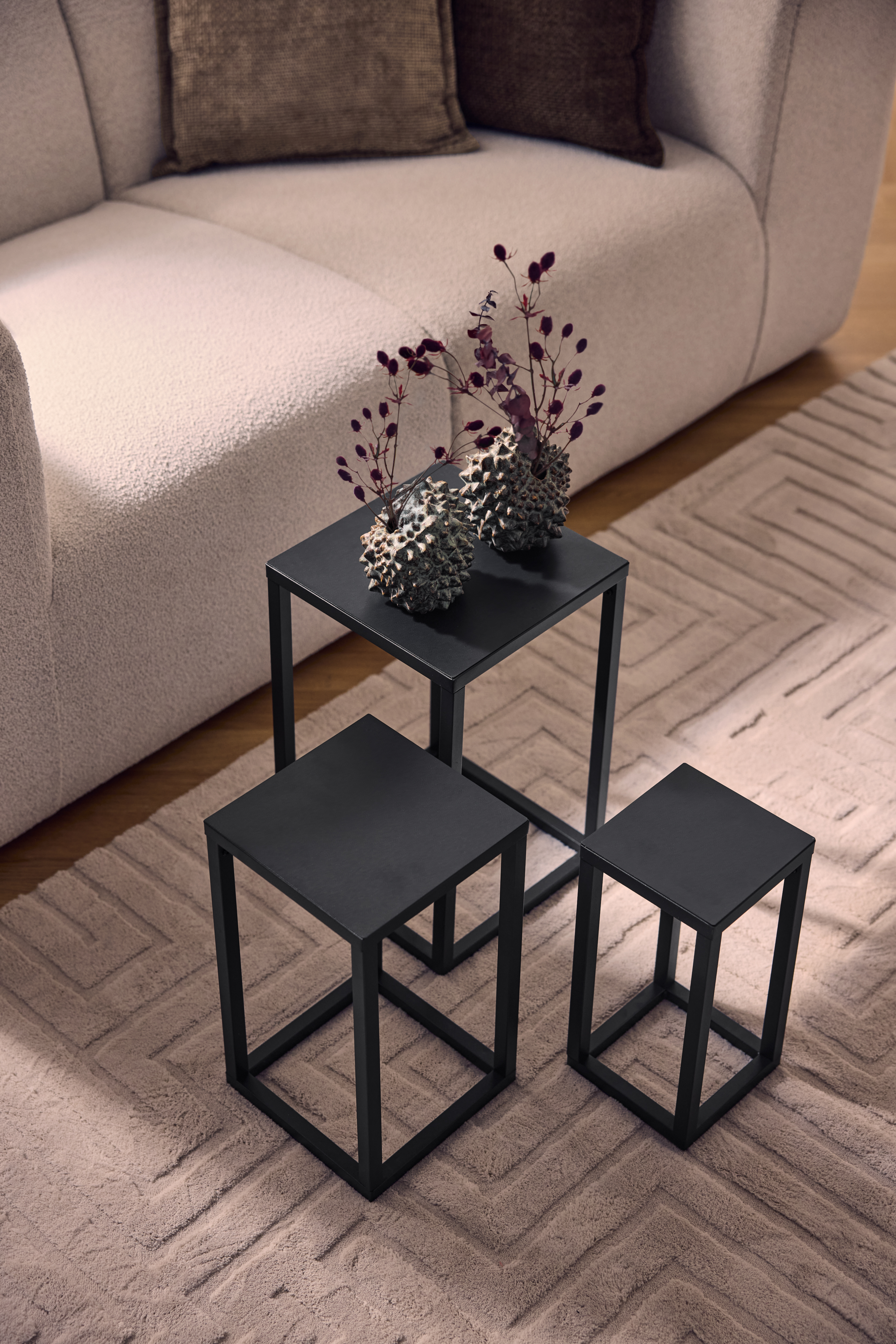 Tre svarta soffbord i metall på en beige matta med geometriskt mönster, bredvid en ljus soffa.