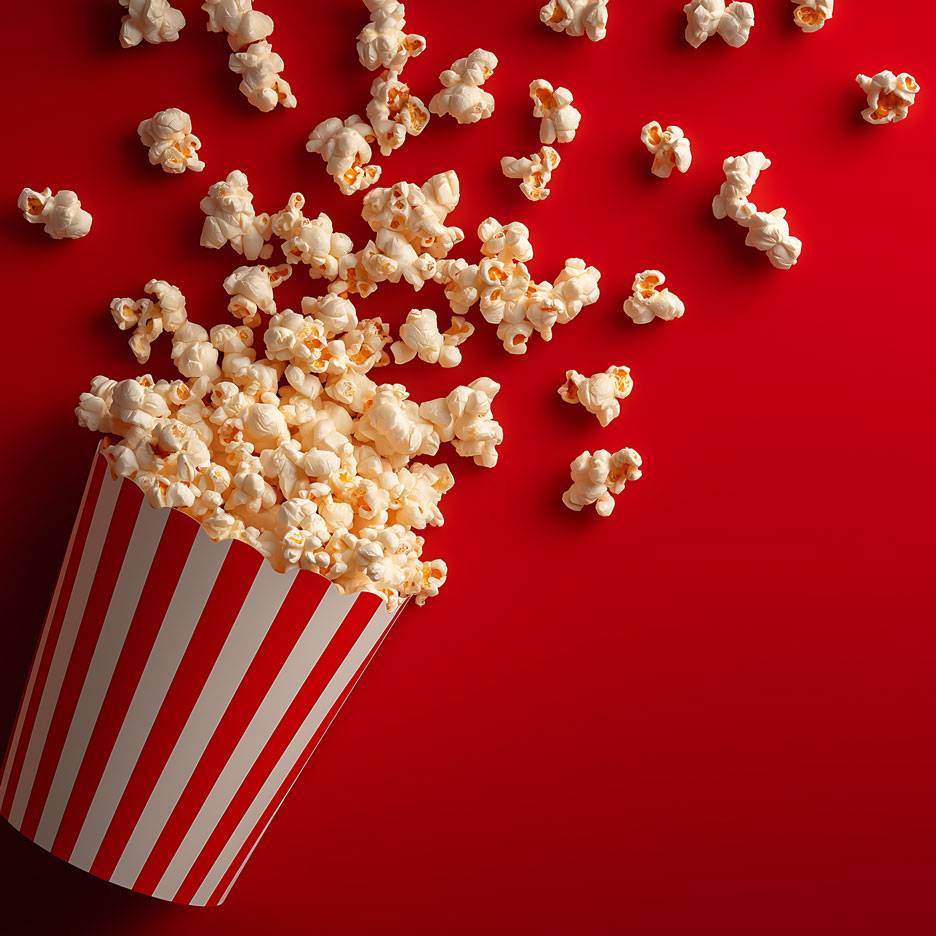 Popcorn på röd bakgrund, en del av popcornen i en randig pappmugg.