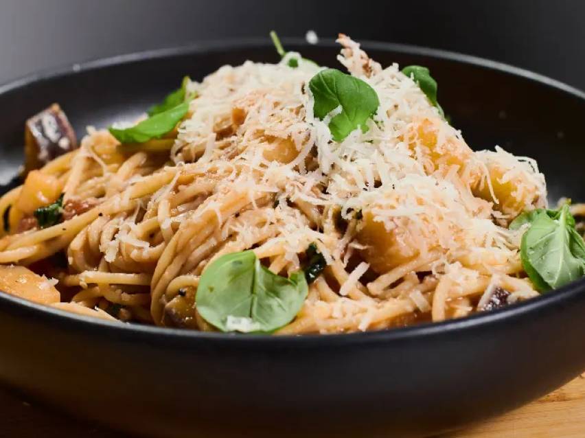 En skål med spaghetti med rostade grönsaker, parmesanost och basilika.