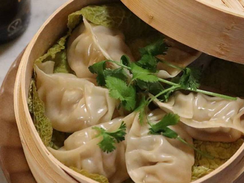 Ångade dumplings serveras i en bambuskorg med koriander.