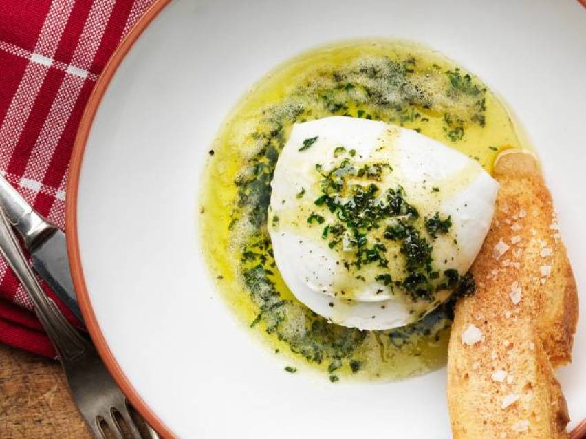 En portion burrata med örtolja och knaprigt bröd på en vit tallrik.