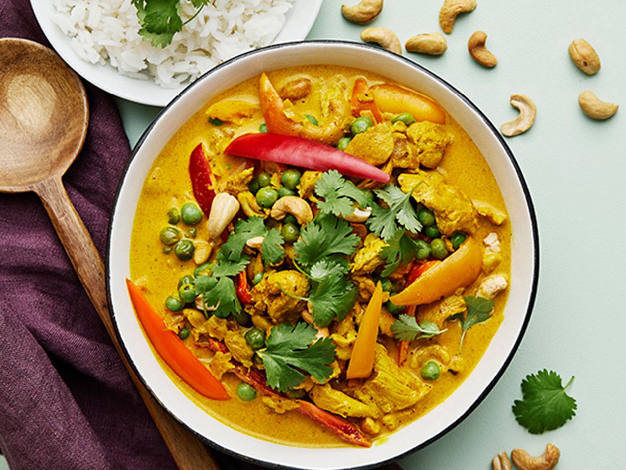 En skål med gul kycklingcurry med ris, cashewnötter och en träsked.