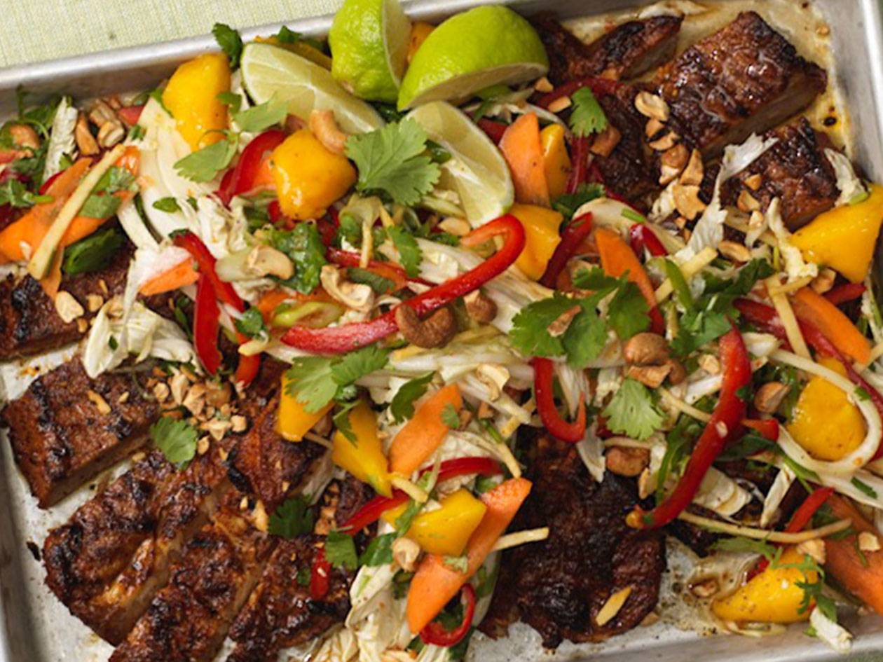 Grillat kött med asiatisk sallad, mango, paprika, morötter och limeklyftor på en plåt.
