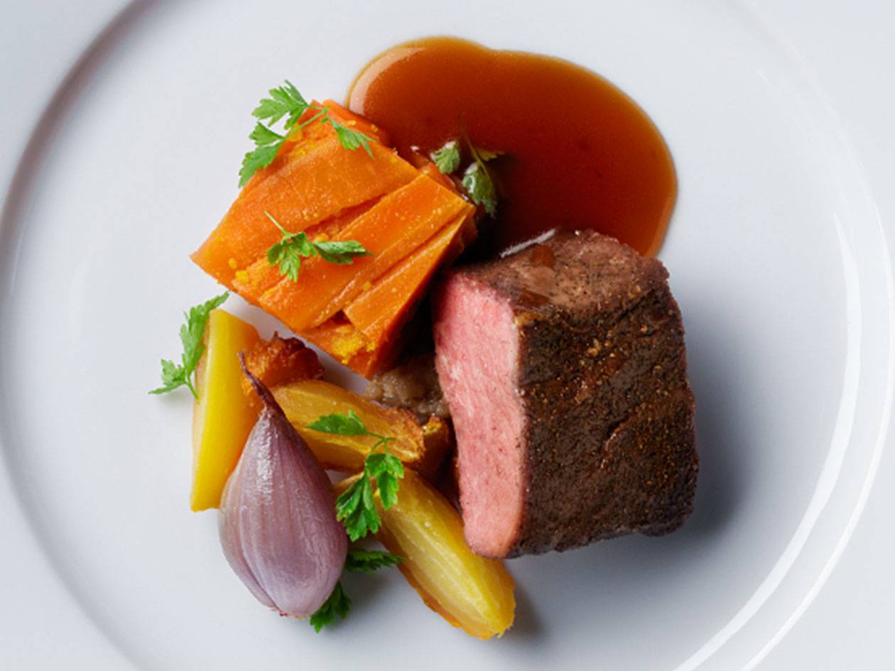 En tallrik med stekt kött, glaserade morötter, lök och en rik sås.