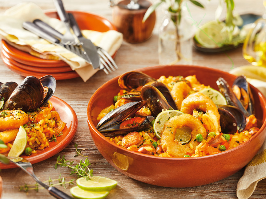 Paella med skaldjur, ris och grönsaker i terrakottaskålar på ett träbord.