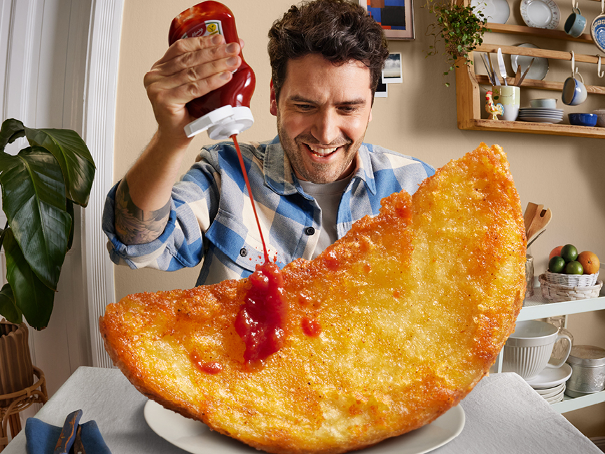Man häller Heinz ketchup på en gigantisk hash brown.
