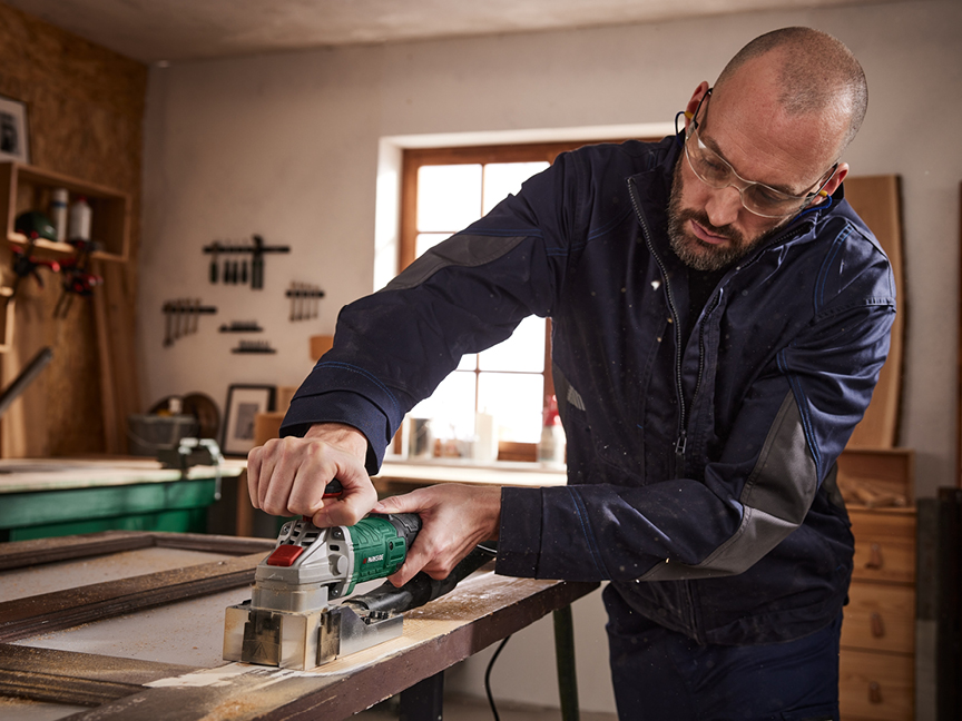 En snickare använder en Bosch-planslip för att slipa en dörr i sin verkstad.