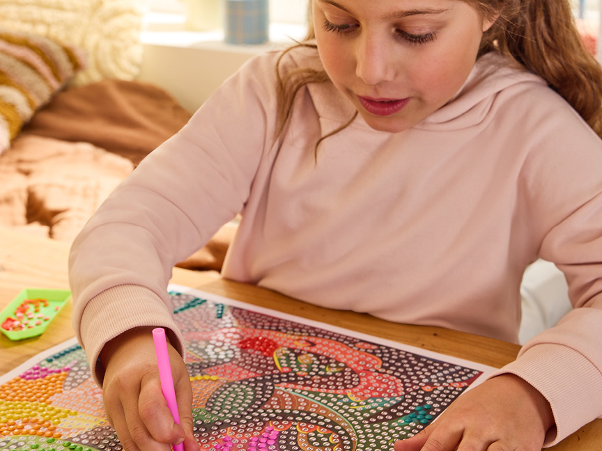 En flicka gör ett diamantmålningsprojekt med en rosa penna.