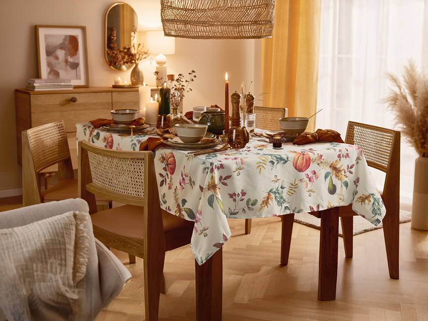 Ett dukat matbord med en höstinspirerad duk, stolar med rottingdetaljer och en skänk.