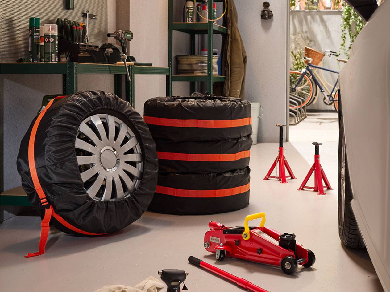 Vinterdäck förpackade med överdrag, hydrauliska domkrafter och bilstöd i ett garage.