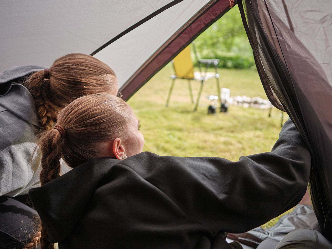 Två flickor tittar ut genom öppningen i ett tält.