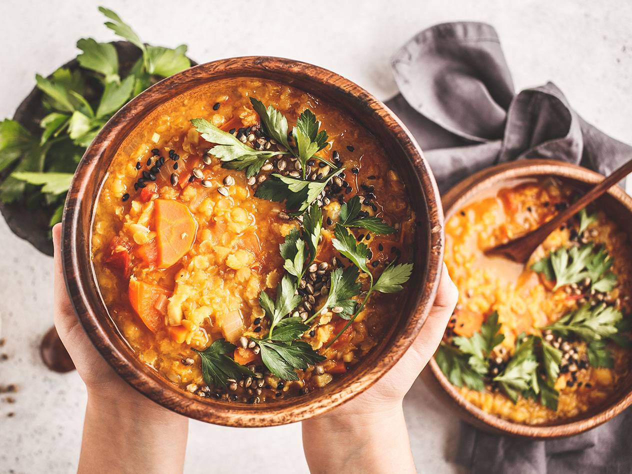 En person håller en skål med linssoppa toppad med persilja och frön, med en liknande skål bredvid.