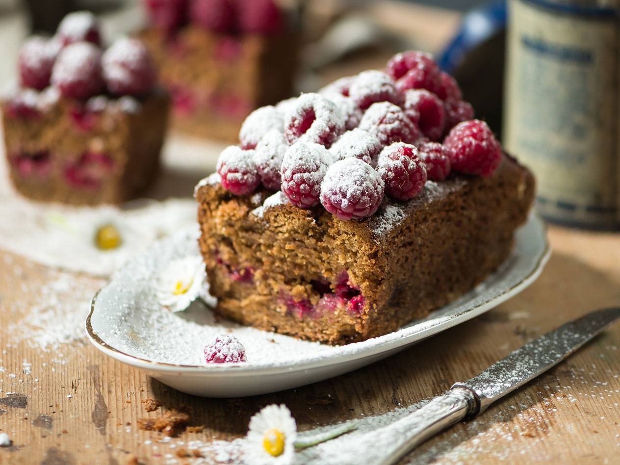 Hallonkaka med florsocker på ett fat, med en kniv och blommor.