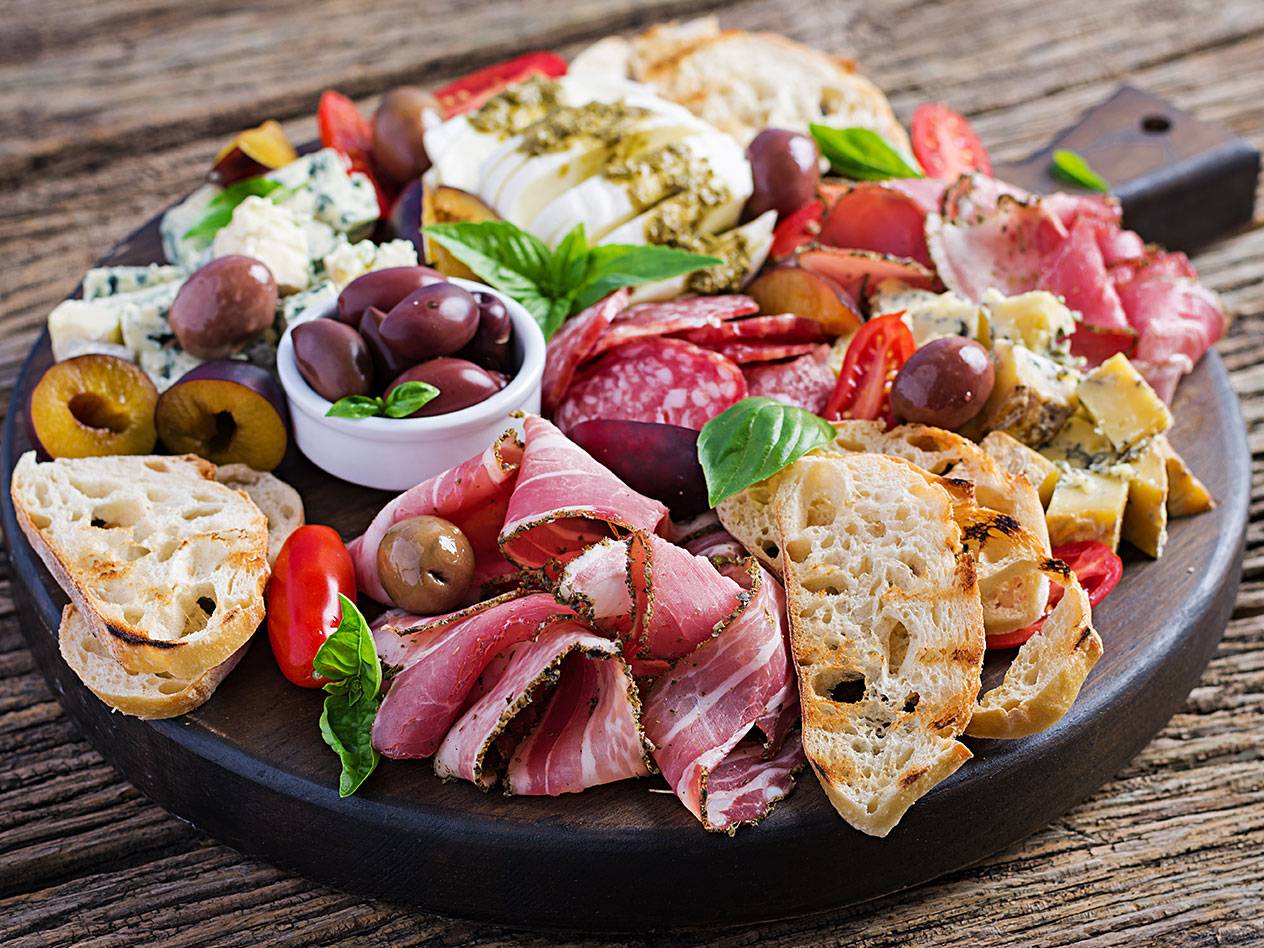 En charkbricka med olika sorters charkuterier, ostar, oliver, bröd och frukt.