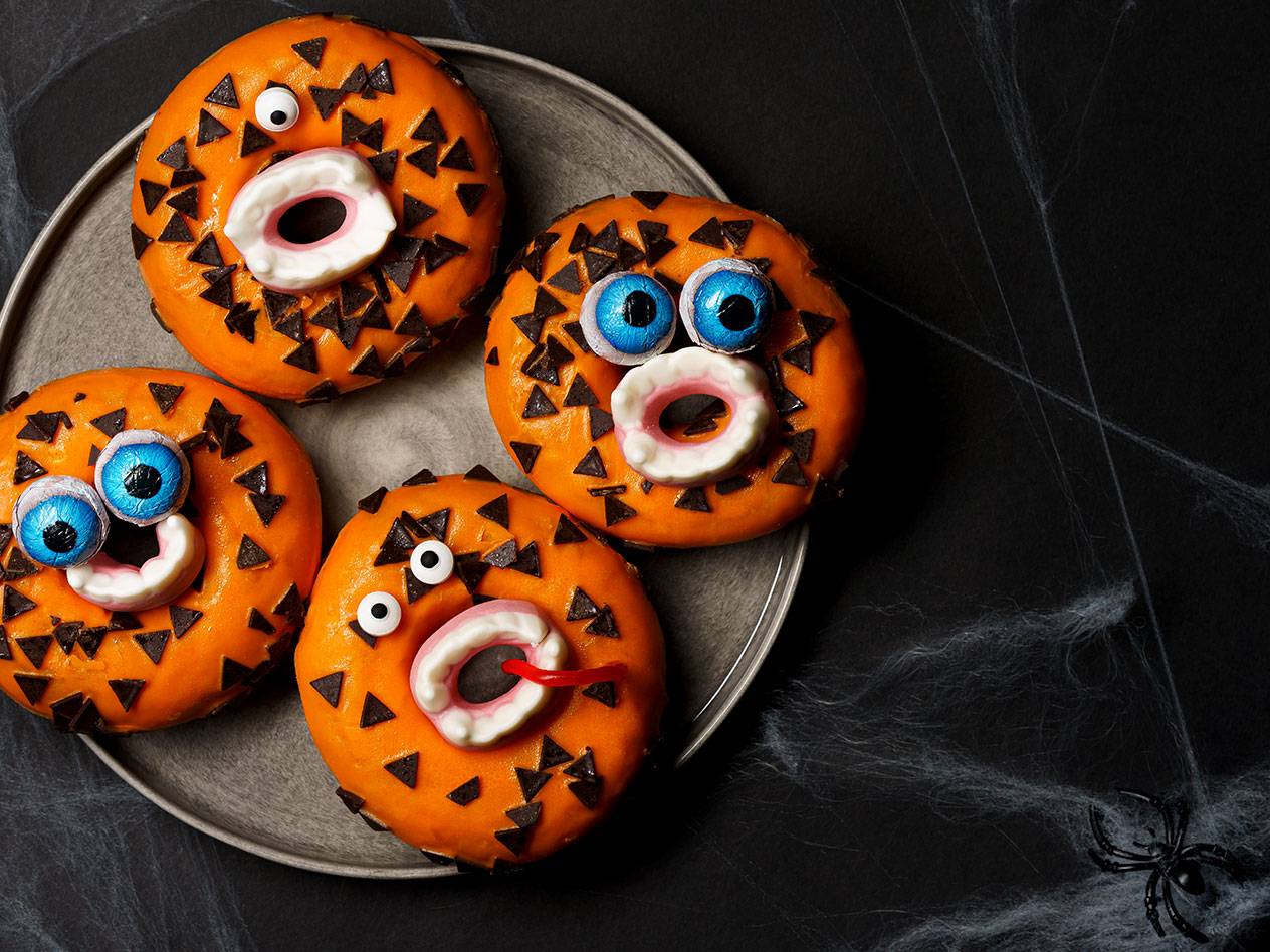 Halloween-munkar med orange glasyr, chokladbitar och godisögon på en tallrik.