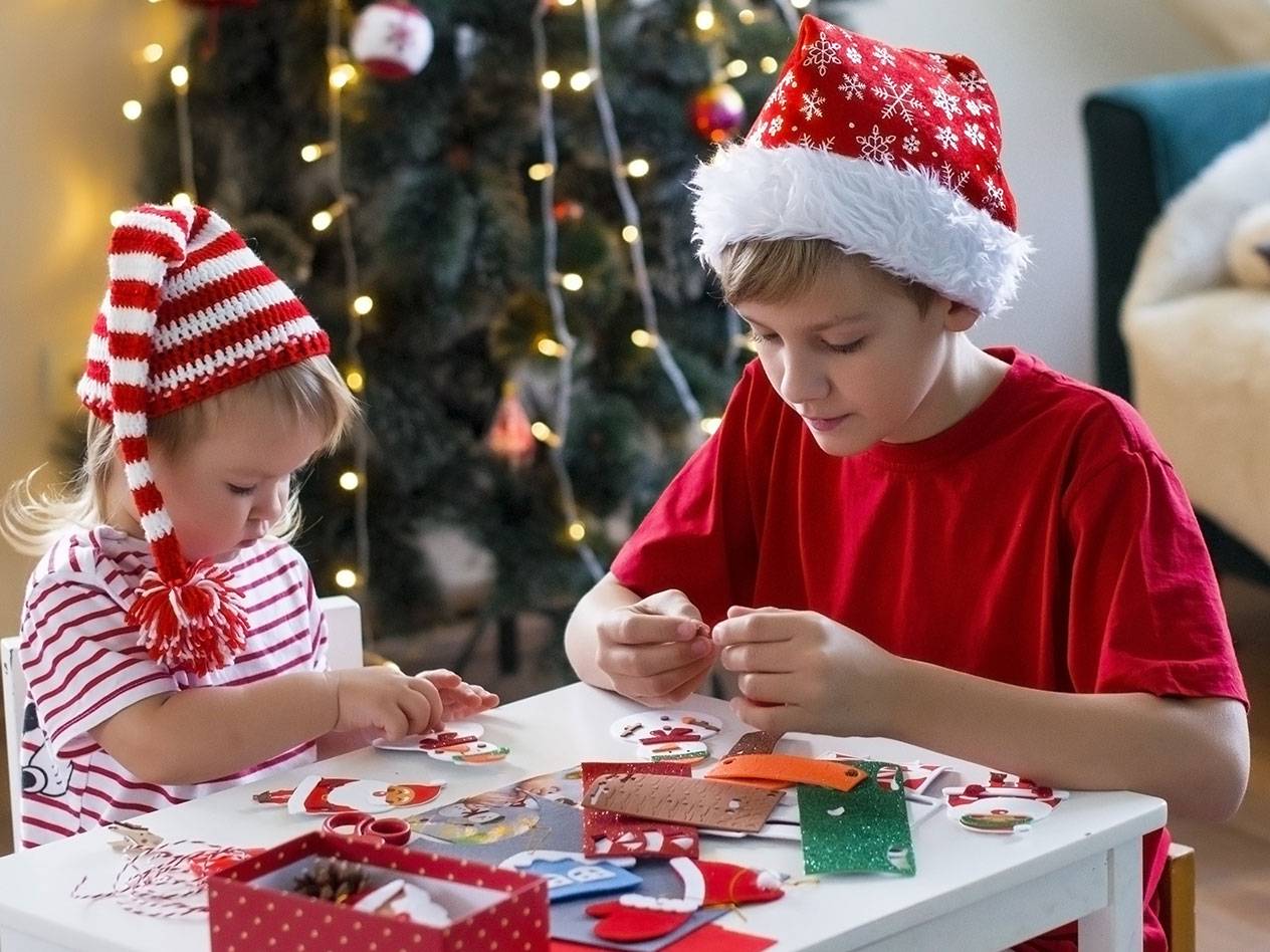 Två barn i tomteluvor pysslar med juldekorationer vid ett bord.