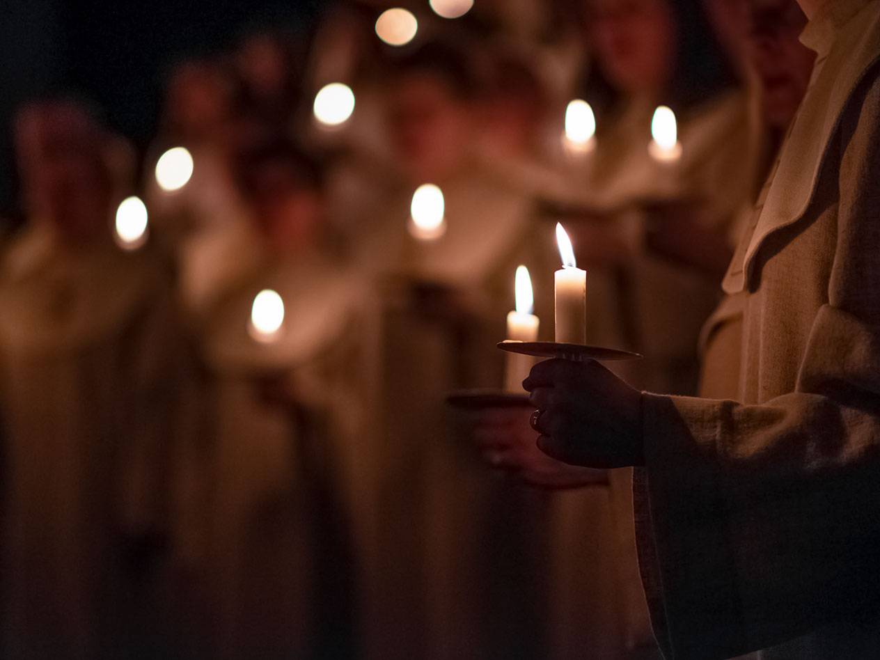 Personer i mörker håller tända ljus, med fler ljus i bakgrunden.