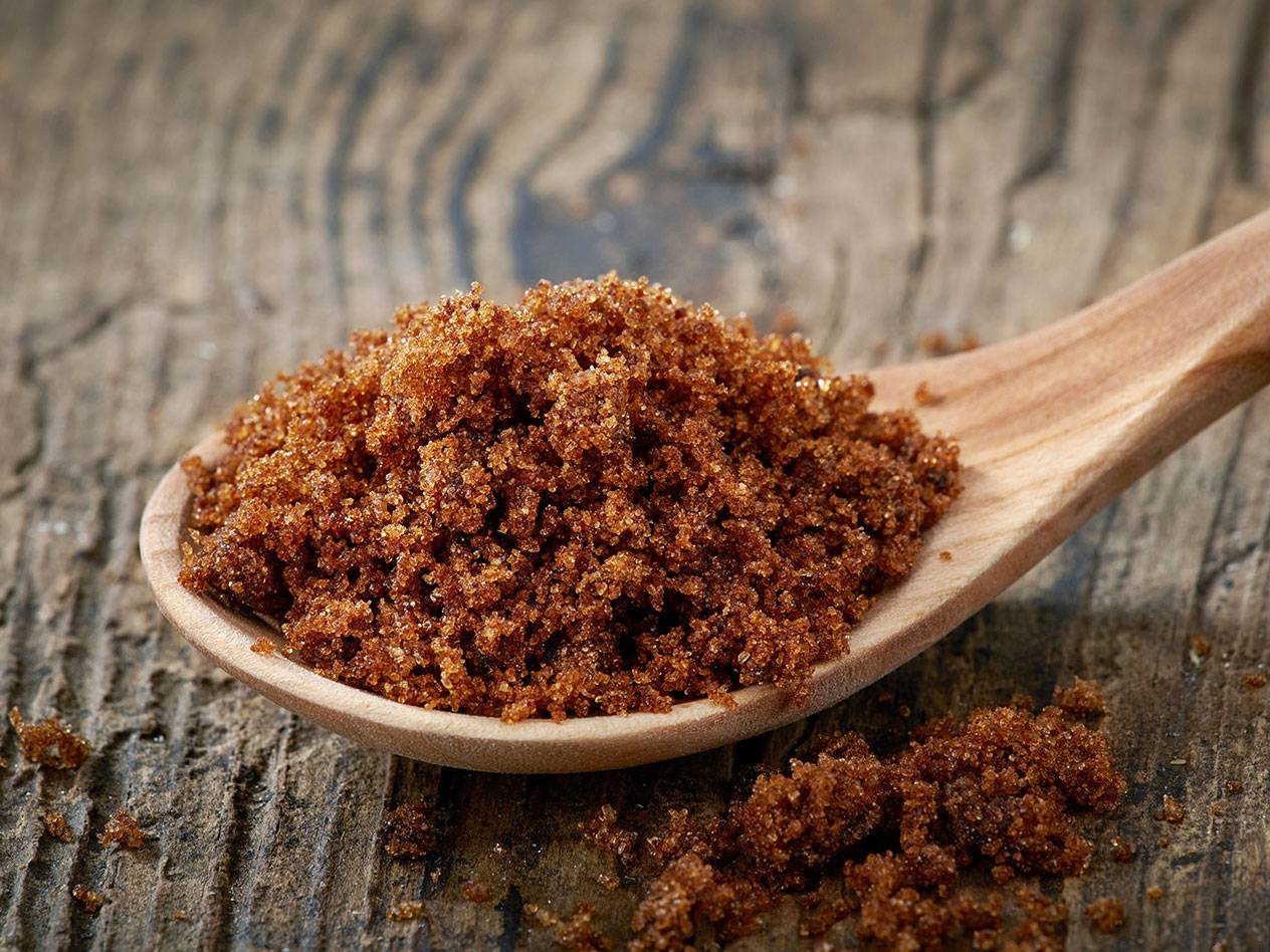 En träslev fylld med brunt socker på en träyta.