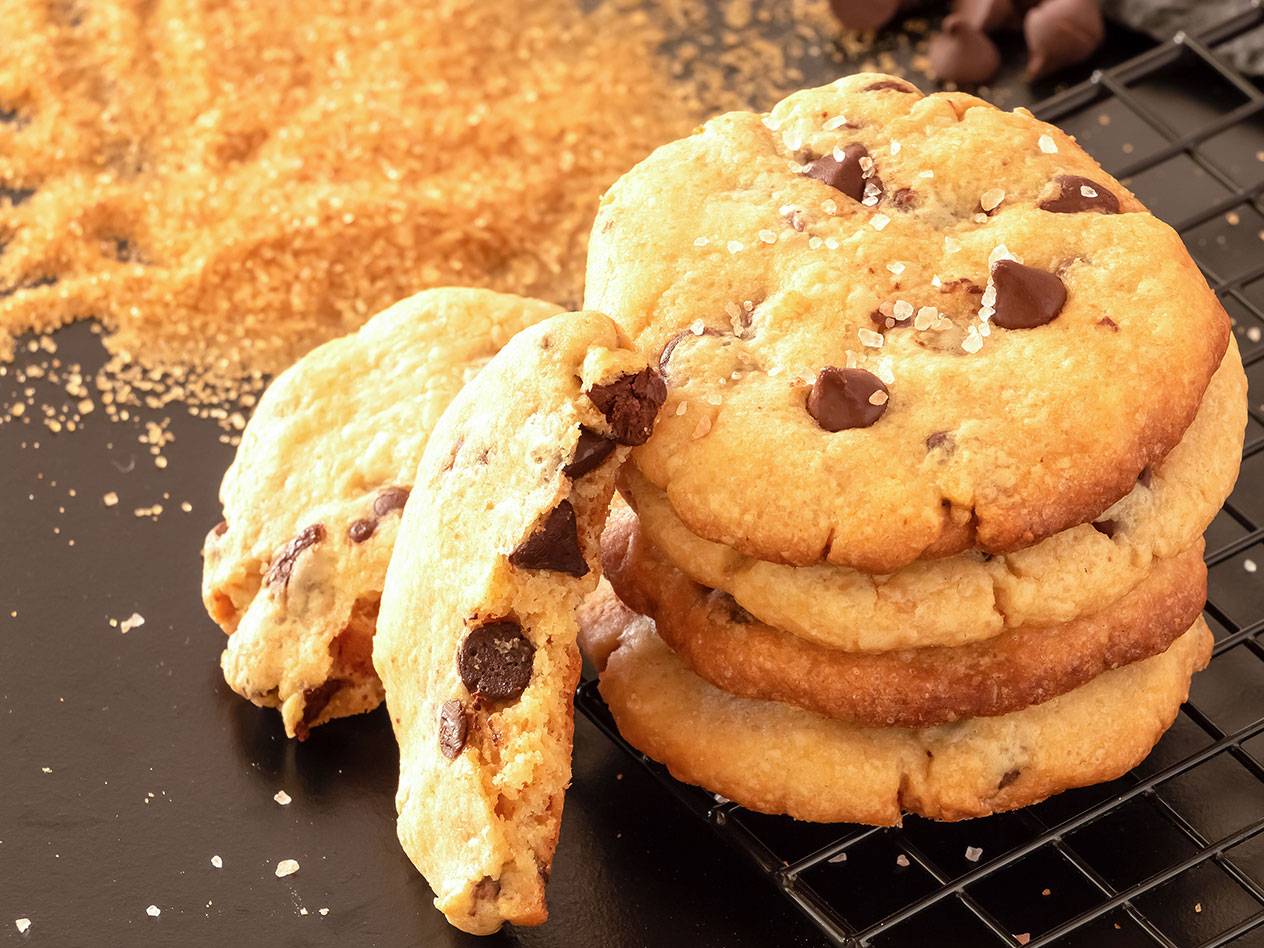 Chokladkakor med havssalt, strösocker och chokladbitar på en svart bakgrund.