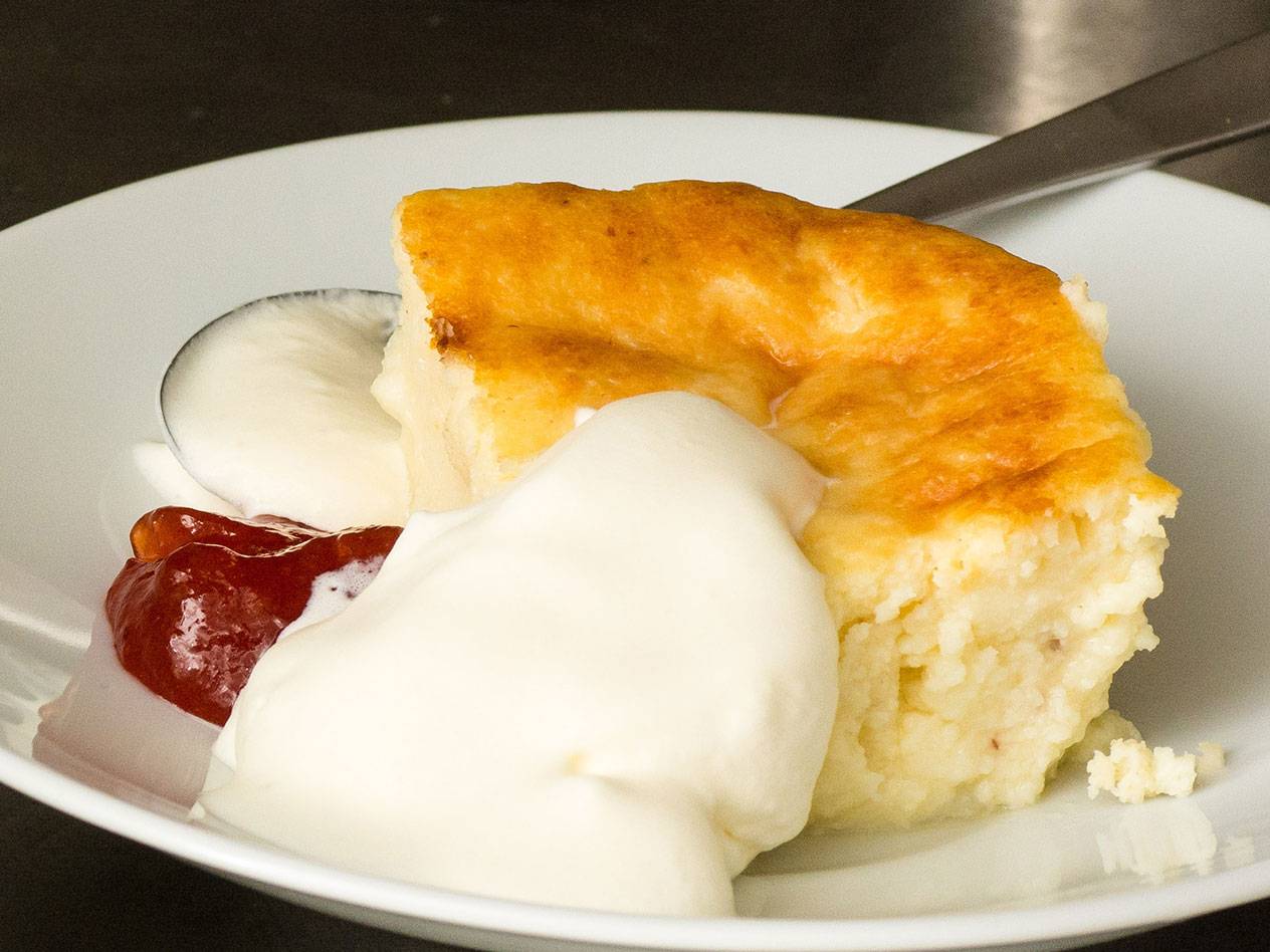 En bit ostkaka med gräddfil och sylt på en vit tallrik.