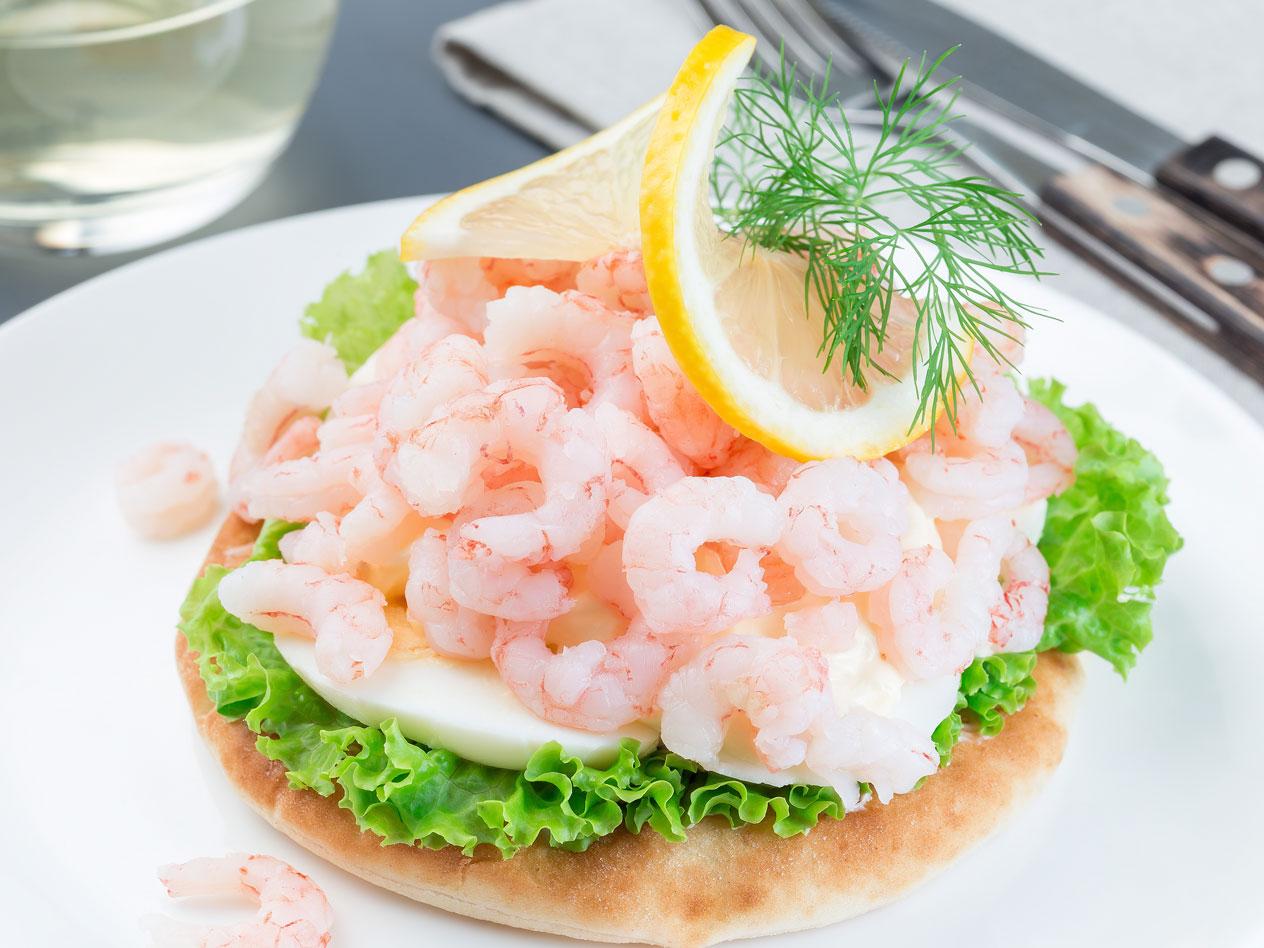 Klassisk räksmörgås med ägg, sallad, citron och dill på en vit tallrik.