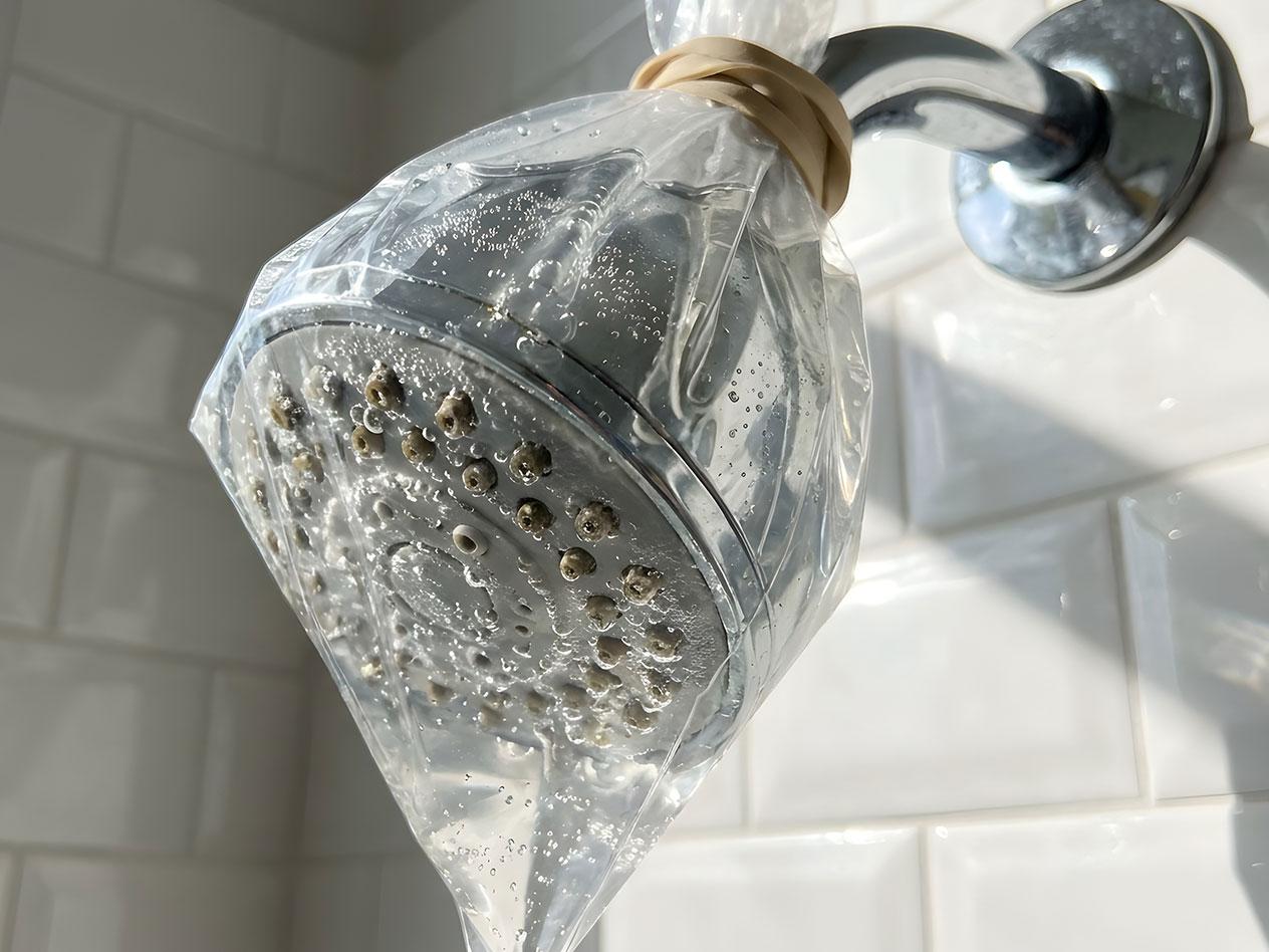 Duschhuvud med en plastpåse fylld med rengöringsmedel för avkalkning.