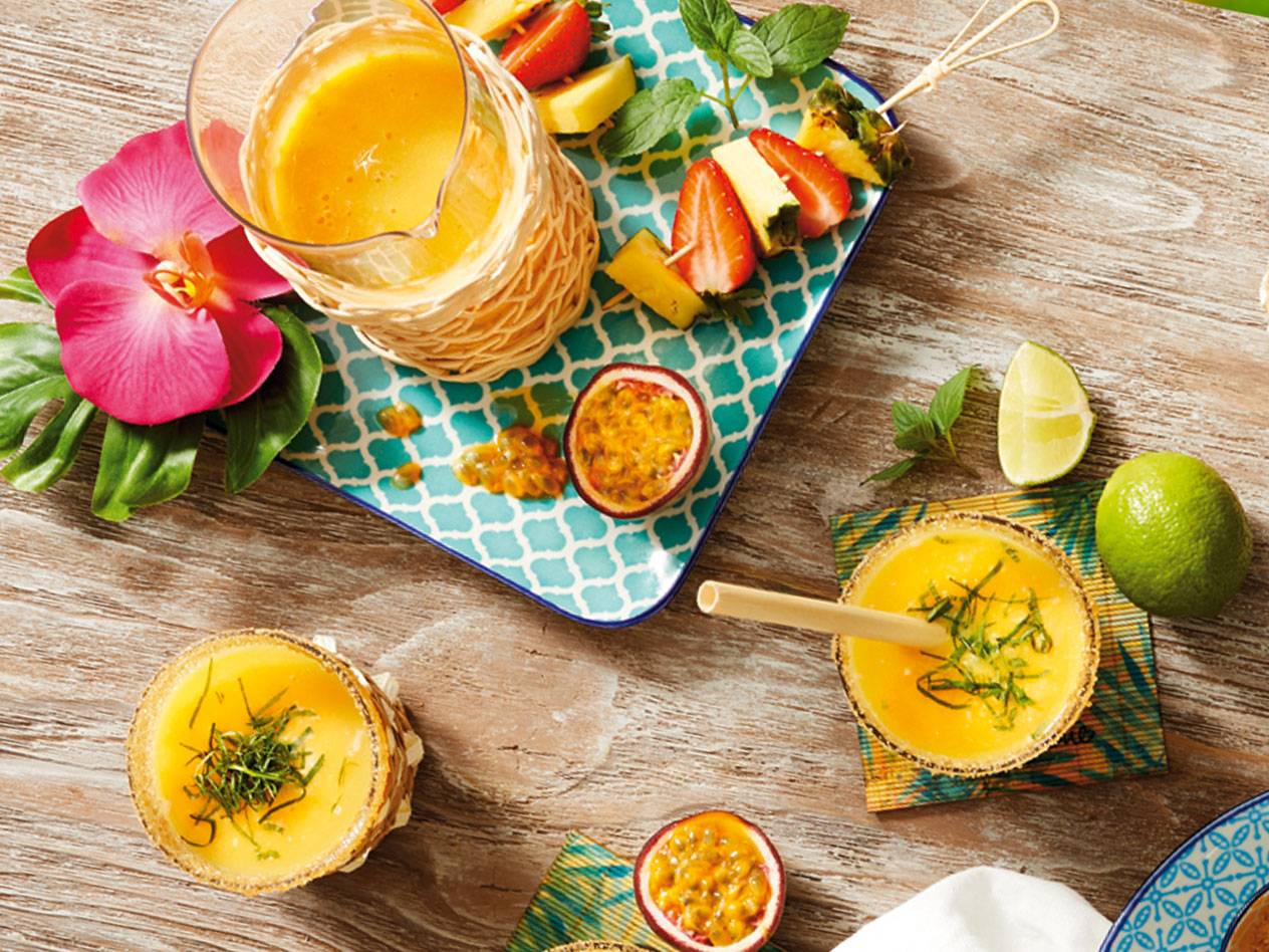 Tropiska drinkar med passionsfrukt, lime och fruktsallad på en träyta.