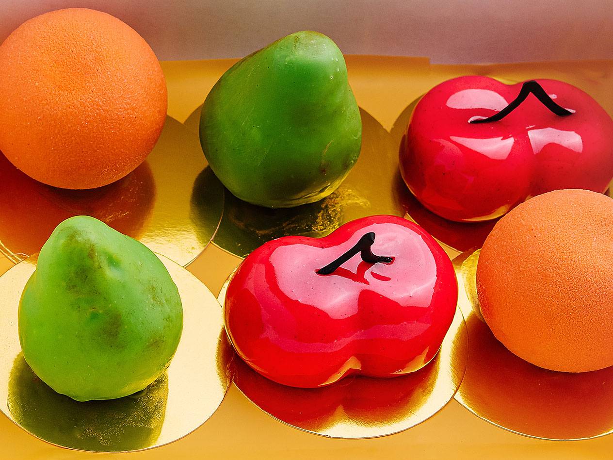 Färgglada marsipanfrukter i form av apelsiner, päron och körsbär på guldbakplåtar.